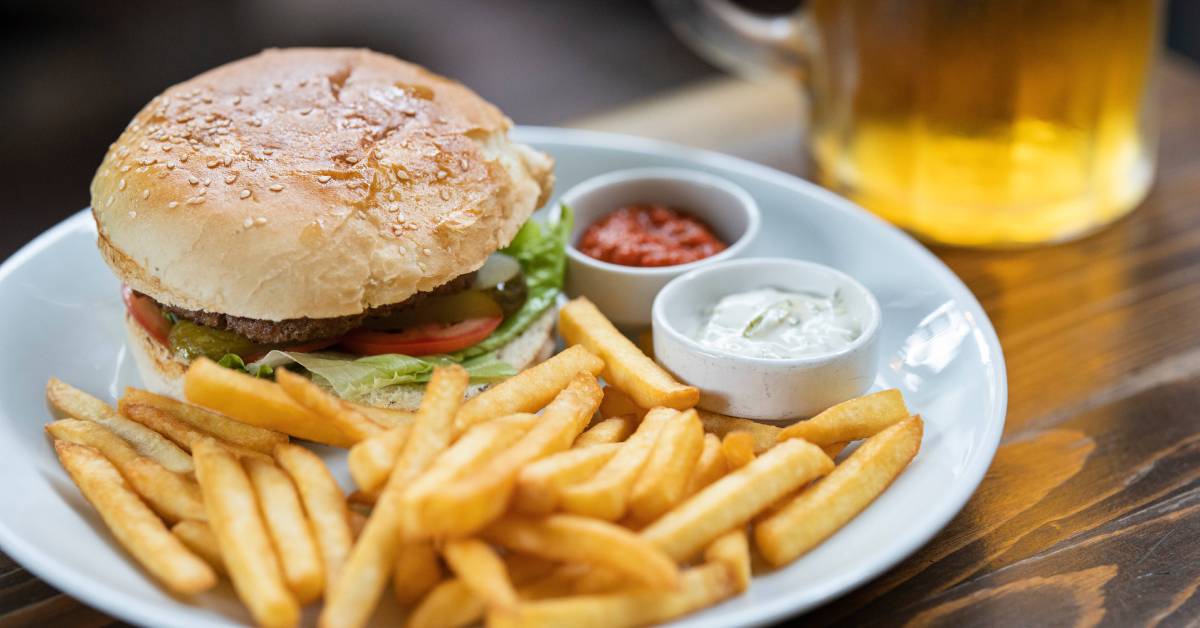 Burger with fries and dipping sauce on a plate beside a glass of beer.